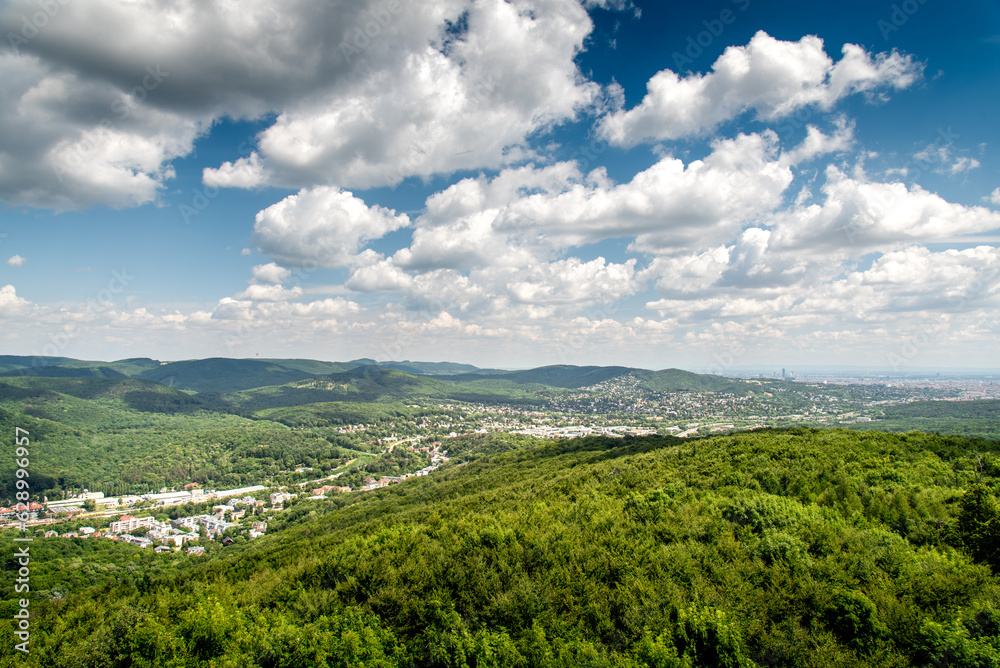 Aerial view on the outskirts of Vienna city in Austria with the beautiful green hills of the Viennese forest and a dramatic sky in the summer 