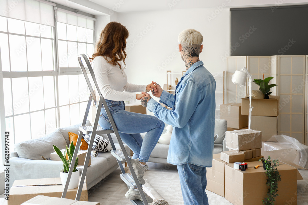Young couple with stepladder in room on moving day