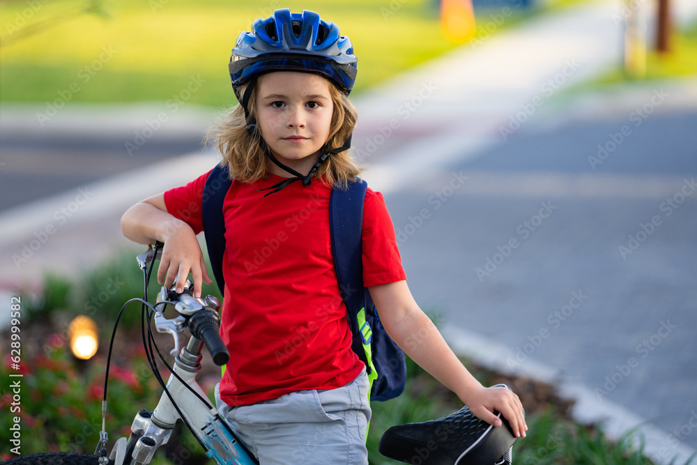 Naklejka premium Child on bicycle. Boy in a helmet riding bike. Little cute caucasian boy in safety helmet riding bike in city park. Child first bike. Kid outdoors summer activities. Kid on bicycle. Boy ride a bike.