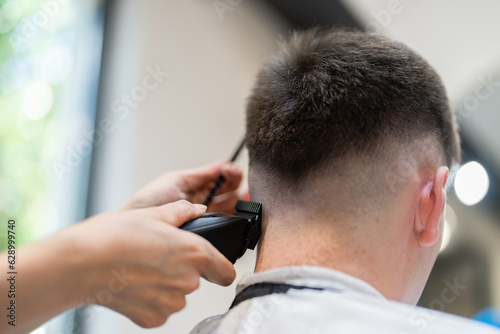 Barber girl cuts a man's hair. Back view of Hairdresser shaving his client's hair with clipper in salon. Self care, masculine beauty. Barber.