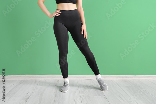Sporty young woman in leggings near green wall