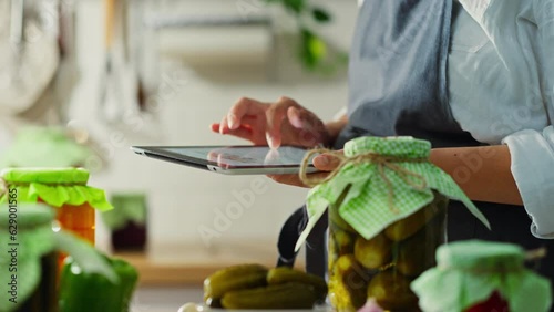 Canning, housewife woman intently Holds an electronic tablet in the housewife's home kitchen. Slow motion farm hostess is at the workplace author's fermented vegetables, cucumber