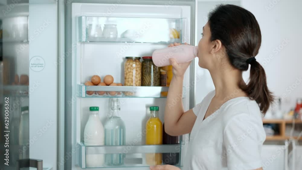Video of beautiful young woman drinking a healthy pink smoothie from the fridge in the kitchen at home Video of beautiful young woman drinking a healthy pink smoothie from the fridge in the kitchen at home