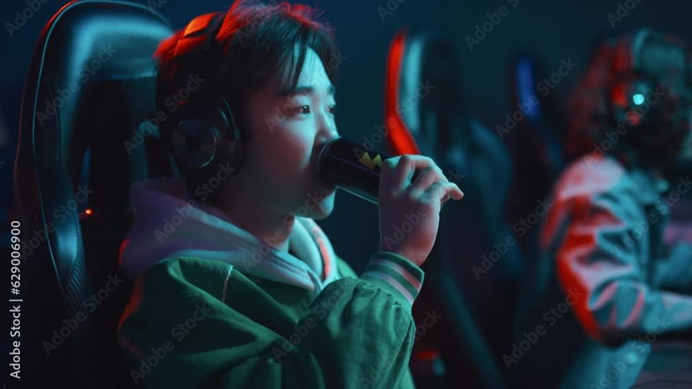 Medium shot of young Asian guy in headset sitting at computer in cyberclub, playing intense video game, finishing level, leaning back on chair and sipping energy drink from can Medium shot of young Asian guy in headset sitting at computer in cyberclub, playing intense video game, finishing level, leaning back on chair and sipping energy drink from can