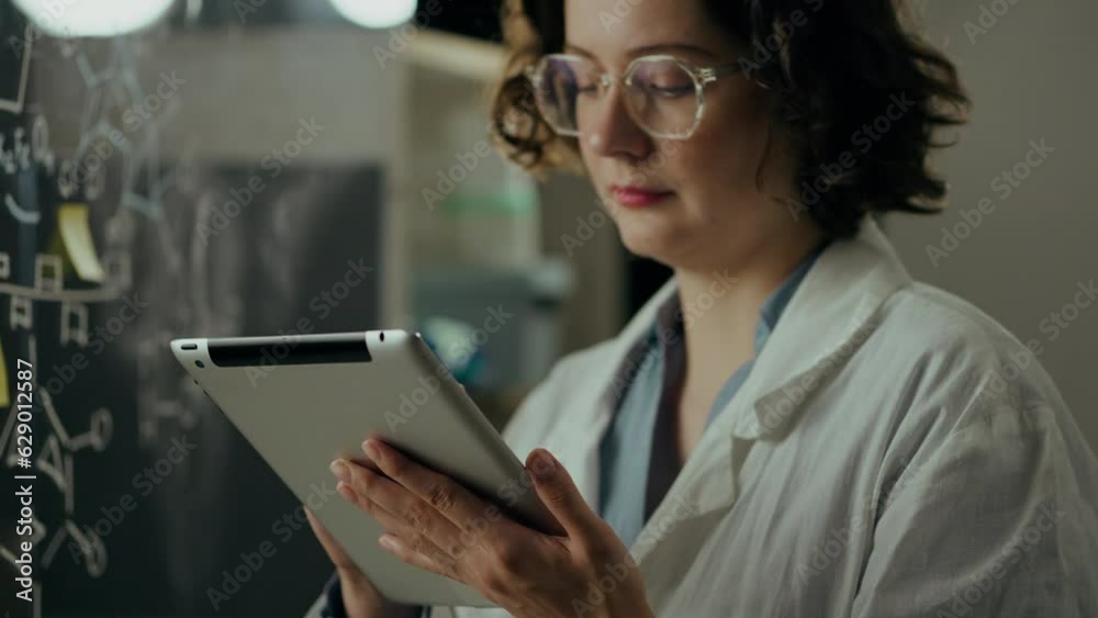 Analysis, Middle-aged woman Focusedly keeps looking at the screen of the tablet checking the data In the research center. Microbiologist Develops a cure for the flu In a modern science center Analysis, Middle-aged woman Focusedly keeps looking at the screen of the tablet checking the data In the research center. Microbiologist Develops a cure for the flu In a modern science center