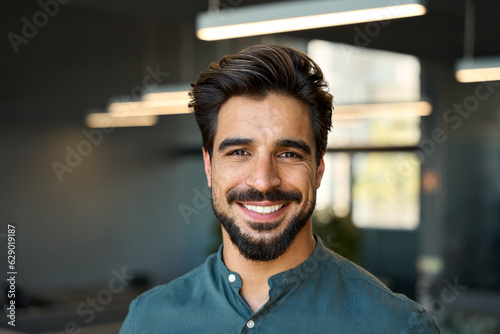 Smiling handsome young business man looking at camera in office, headshot close up corporate portrait. Happy Latin businessman, male entrepreneur, professional manager or company employee at work. photo