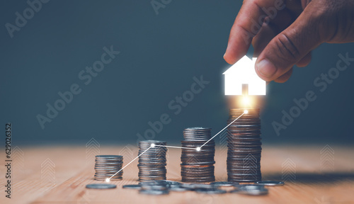 Fotografia Investment for real estate concept, Businessman's hand putting house icon on top of coins stack and progressing graph, Savings money for buy house, budgeting, investment for the future