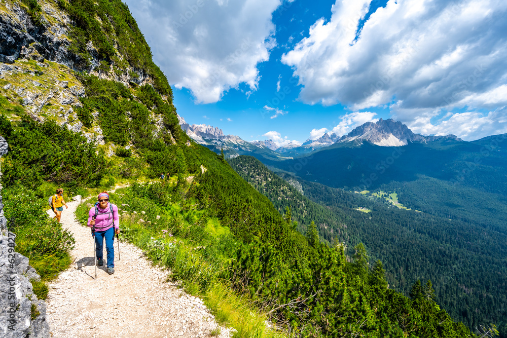 Young woman is walking alongt hiking trail to Sorapis lake with  beautiful view on Monte Cristallo in the morning. Lake Sorapis, Dolomites, Belluno, Italy, Europe.