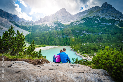 Young sportive couple enjoys view on the turquoise Sorapis lake from a beautiful restpoint in the afternoon. Lake Sorapis, Dolomites, Belluno, Italy, Europe.