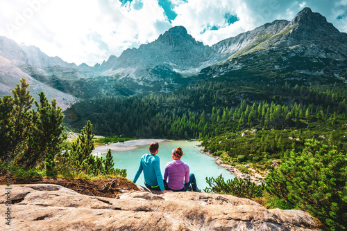 Young sportive couple enjoys view on the turquoise Sorapis lake from a beautiful restpoint in the afternoon. Lake Sorapis, Dolomites, Belluno, Italy, Europe.