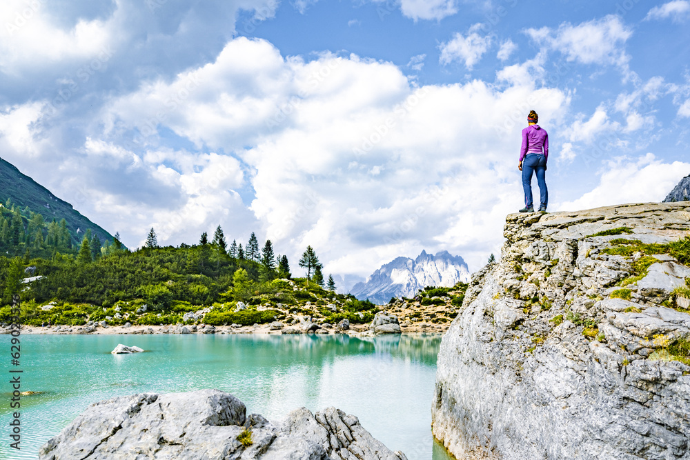 Young sportive woman enjoys view on the turquoise Sorapis lake from a big boulder block in the afternoon. Lake Sorapis, Dolomites, Belluno, Italy, Europe.