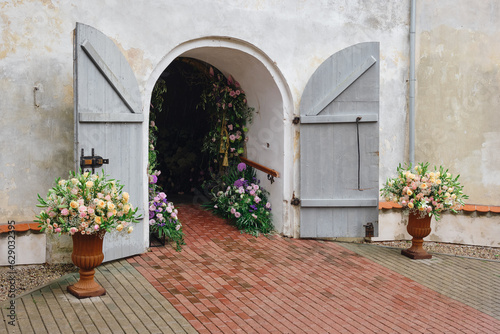 Fototapeta Naklejka Na Ścianę i Meble -  The entrance to the building is beautifully and elegantly decorated with flowers for the holiday. Open doors to the church for the wedding ceremony.