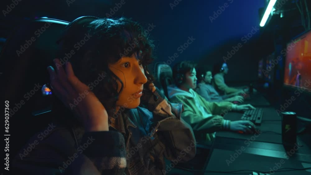 Medium close-up slowmo shot of young biracial female gamer putting on headset and adjusting microphone before entering multiplayer first person shooter video game