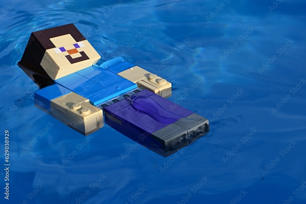 Fototapeta premium LEGO Minecraft figure of Steve swimming backstroke in swimming pool with azure blue floor.