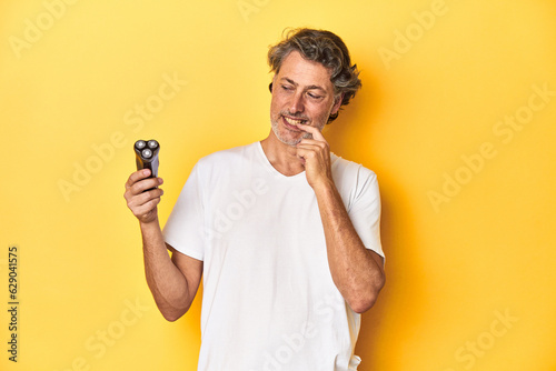 Man holding a razor, yellow studio background relaxed thinking about something looking at a copy space. photo