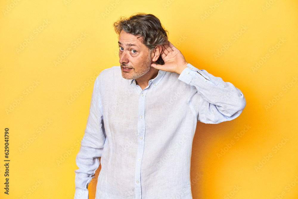 Middle-aged man posing on a yellow backdrop trying to listening a gossip. Middle-aged man posing on a yellow backdrop trying to listening a gossip.