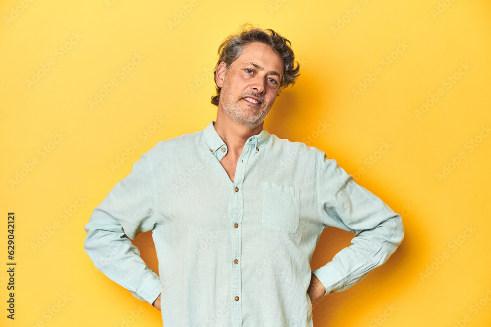 Middle-aged man posing on a yellow backdrop confident keeping hands on hips. Middle-aged man posing on a yellow backdrop confident keeping hands on hips.