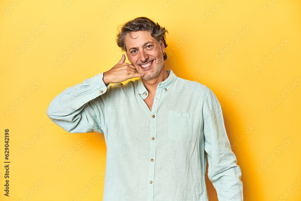 Middle-aged man posing on a yellow backdrop showing a mobile phone call gesture with fingers. Middle-aged man posing on a yellow backdrop showing a mobile phone call gesture with fingers.