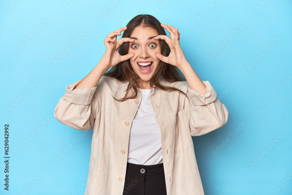 Stylish young woman in an overshirt on a blue background keeping eyes opened to find a success opportunity. Stylish young woman in an overshirt on a blue background keeping eyes opened to find a success opportunity.