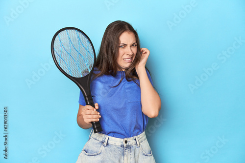 Tableau sur toile Woman with an electric bug zapper on a blue background covering ears with hands