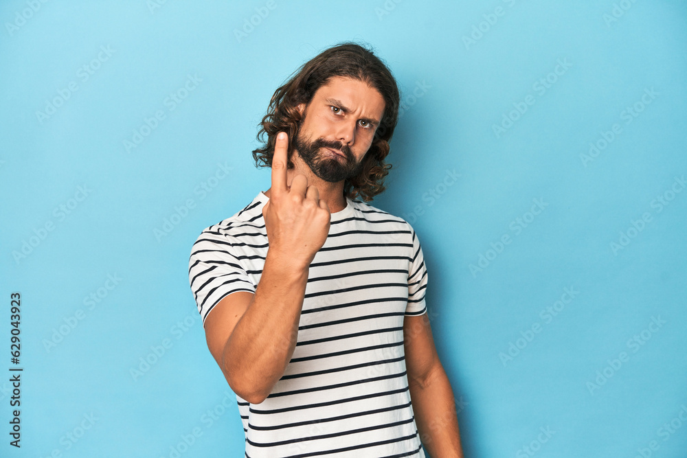 Bearded man in a striped shirt, blue backdrop pointing with finger at you as if inviting come closer. Bearded man in a striped shirt, blue backdrop pointing with finger at you as if inviting come closer.