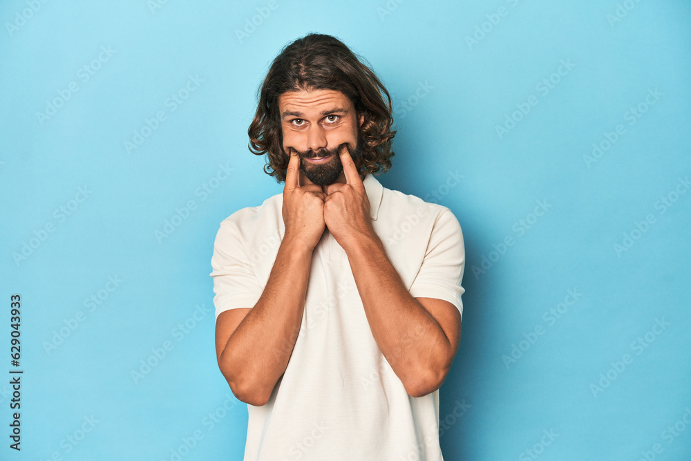 Long-haired man in a white polo, blue studio doubting between two options. Long-haired man in a white polo, blue studio doubting between two options.