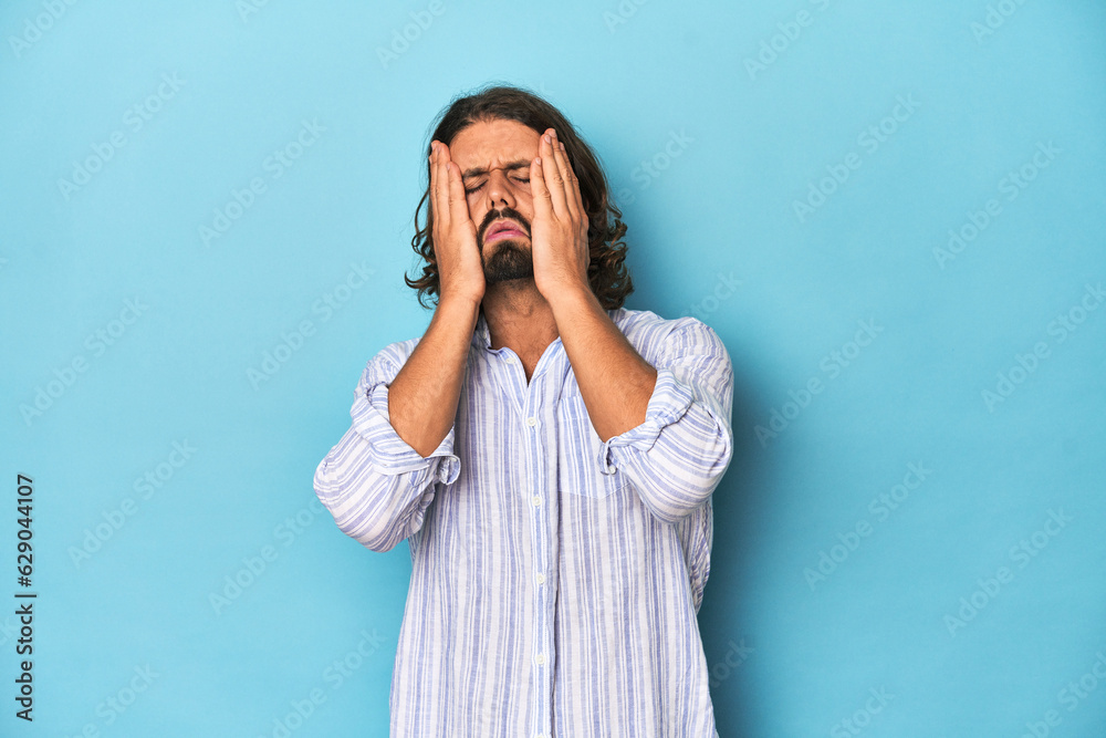 Man with beard in blue striped shirt, blue studio crying, unhappy with something, agony and confusion concept. Man with beard in blue striped shirt, blue studio crying, unhappy with something, agony and confusion concept.