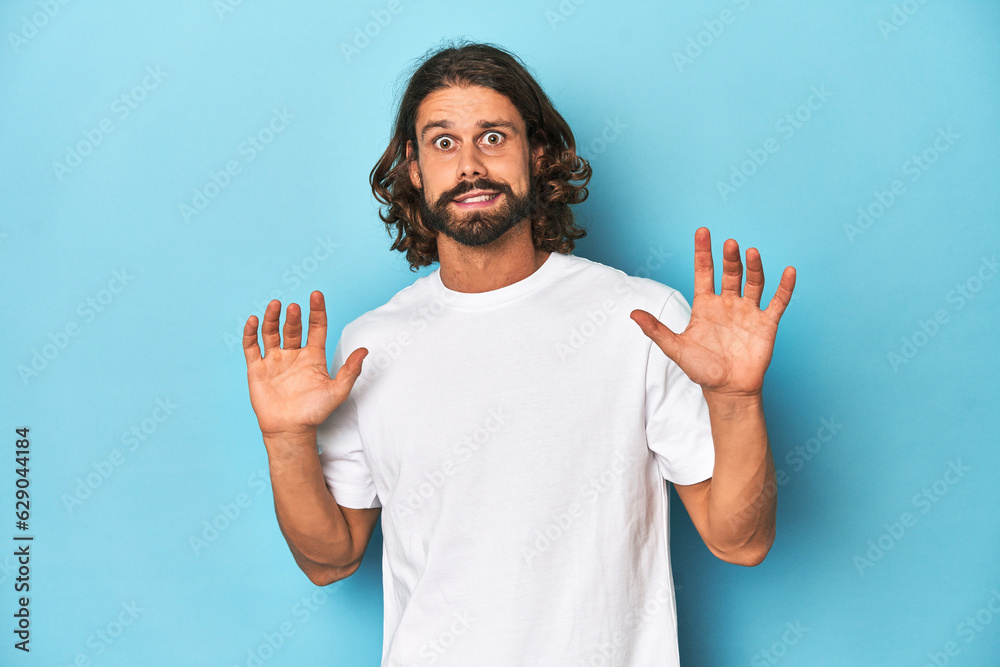 Bearded man in a white shirt, blue backdrop rejecting someone showing a gesture of disgust. Bearded man in a white shirt, blue backdrop rejecting someone showing a gesture of disgust.