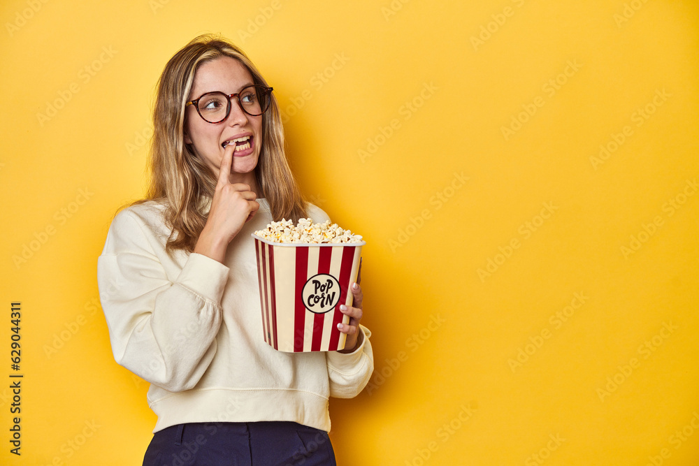 Young Caucasian holding popcorn, cinema concept on yellow backdrop, relaxed thinking about something looking at a copy space. Young Caucasian holding popcorn, cinema concept on yellow backdrop, relaxed thinking about something looking at a copy space.