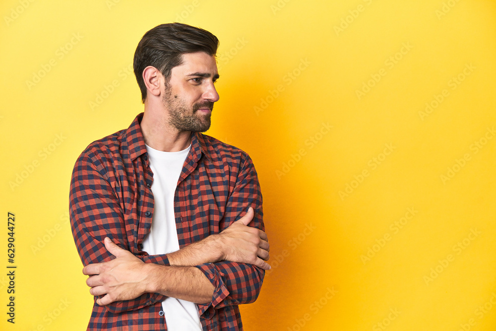 Caucasian man in red checkered shirt, yellow backdrop smiling confident with crossed arms. Caucasian man in red checkered shirt, yellow backdrop smiling confident with crossed arms.