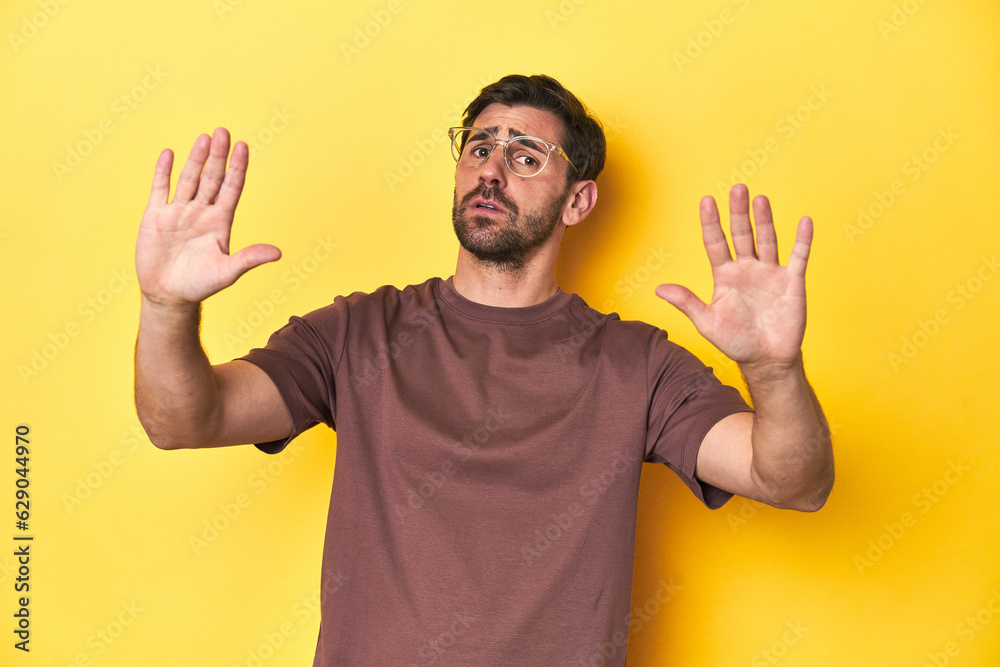 Man making a stop gesture on a yellow studio background. - obrazy, fototapety, plakaty 
