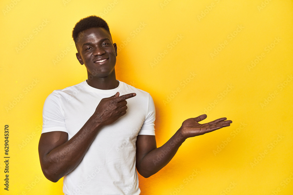 Stylish young African man on vibrant yellow studio background, excited holding a copy space on palm. Stylish young African man on vibrant yellow studio background, excited holding a copy space on palm.