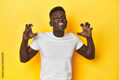 Stylish young African man on vibrant yellow studio background, screaming with rage.