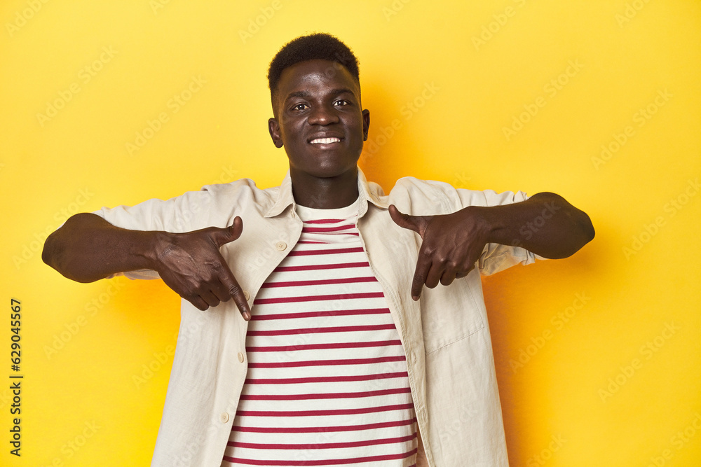 Stylish young African man on vibrant yellow studio background, points down with fingers, positive feeling. Stylish young African man on vibrant yellow studio background, points down with fingers, positive feeling.
