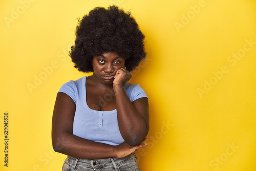African-American woman with afro, studio yellow background who feels sad and pensive, looking at copy space. © Asier