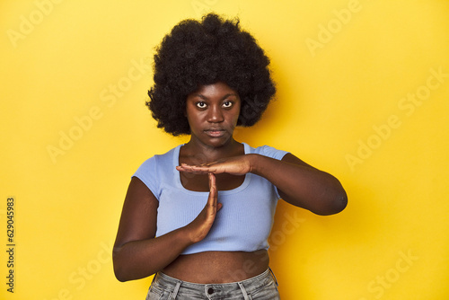 African-American woman with afro, studio yellow background showing a timeout gesture.