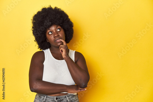 African-American woman with afro, studio yellow background looking sideways with doubtful and skeptical expression. © Asier