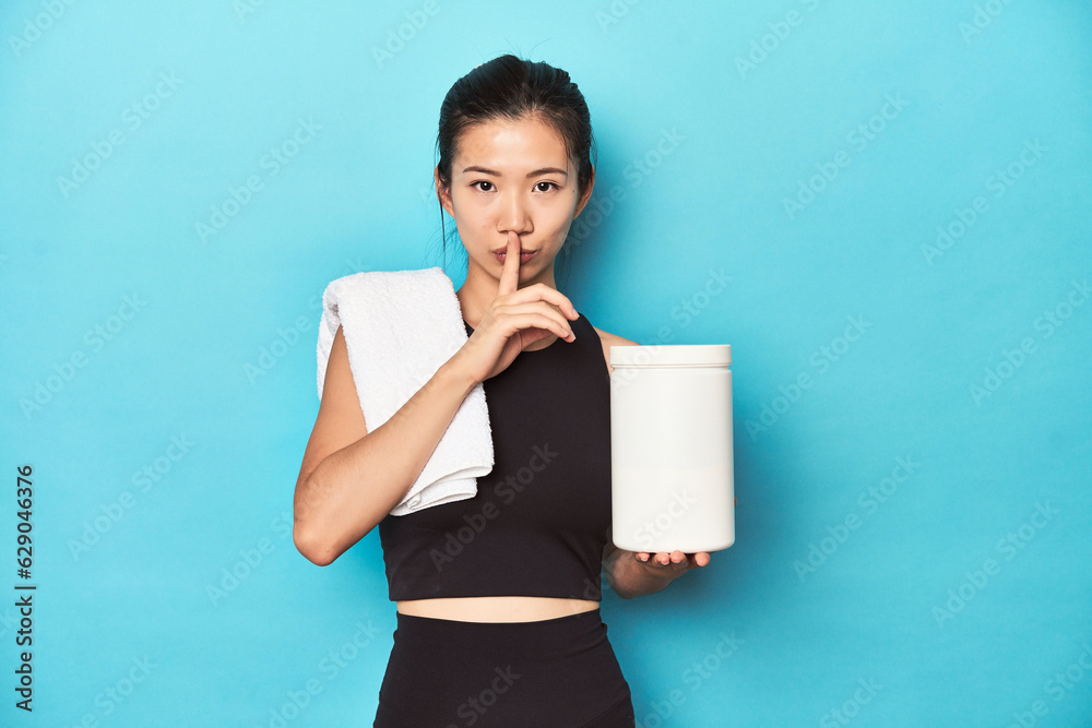 Young Asian sportswoman with protein bottle, gym setup, keeping a secret or asking for silence.