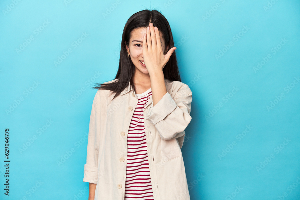 Asian woman in layered shirt and striped t-shirt, having fun covering half of face with palm. Asian woman in layered shirt and striped t-shirt, having fun covering half of face with palm.