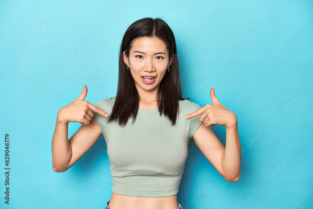 Asian woman in summer green top, studio backdrop, surprised pointing with finger, smiling broadly. Asian woman in summer green top, studio backdrop, surprised pointing with finger, smiling broadly.