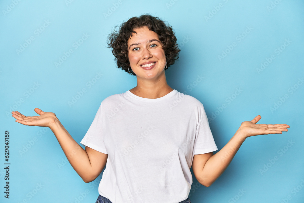 Young Caucasian woman with short hair makes scale with arms, feels happy and confident. Young Caucasian woman with short hair makes scale with arms, feels happy and confident.