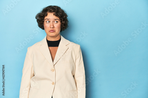 Young woman in elegant white blazer confused, feels doubtful and unsure.