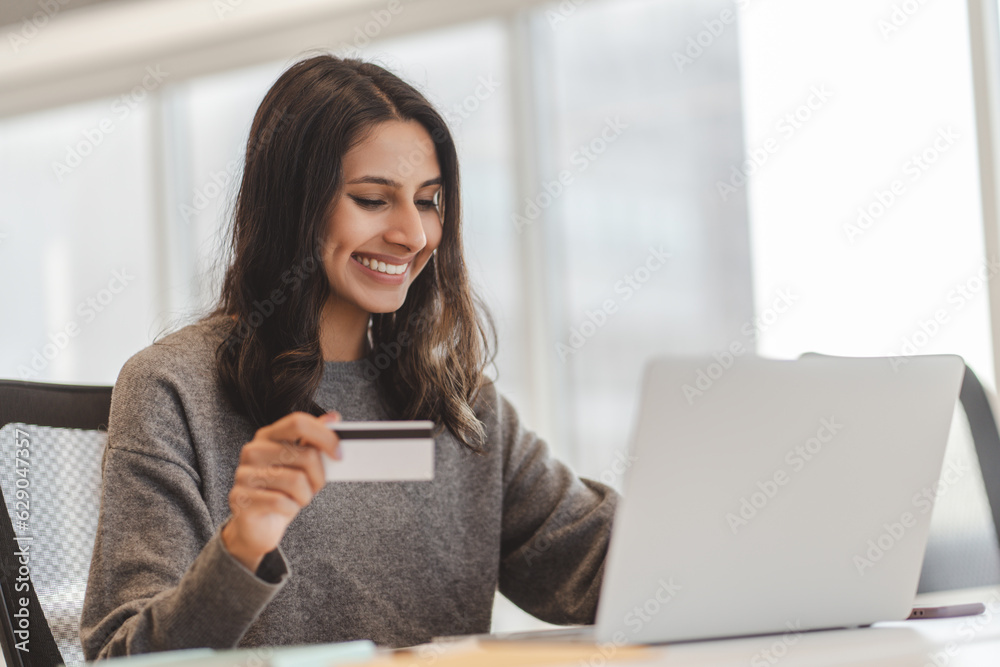 Glad indian woman holding credit card while inputs card number, make online transaction Glad indian woman holding credit card while inputs card number, make online transaction