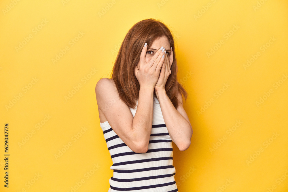 Redhead in a tank top, casual studio shot blink through fingers frightened and nervous. Redhead in a tank top, casual studio shot blink through fingers frightened and nervous.