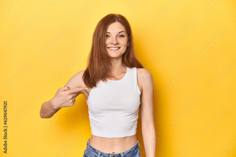 Redhead in white tank top, relaxed studio pose person pointing by hand to a shirt copy space, proud and confident Redhead in white tank top, relaxed studio pose person pointing by hand to a shirt copy space, proud and confident