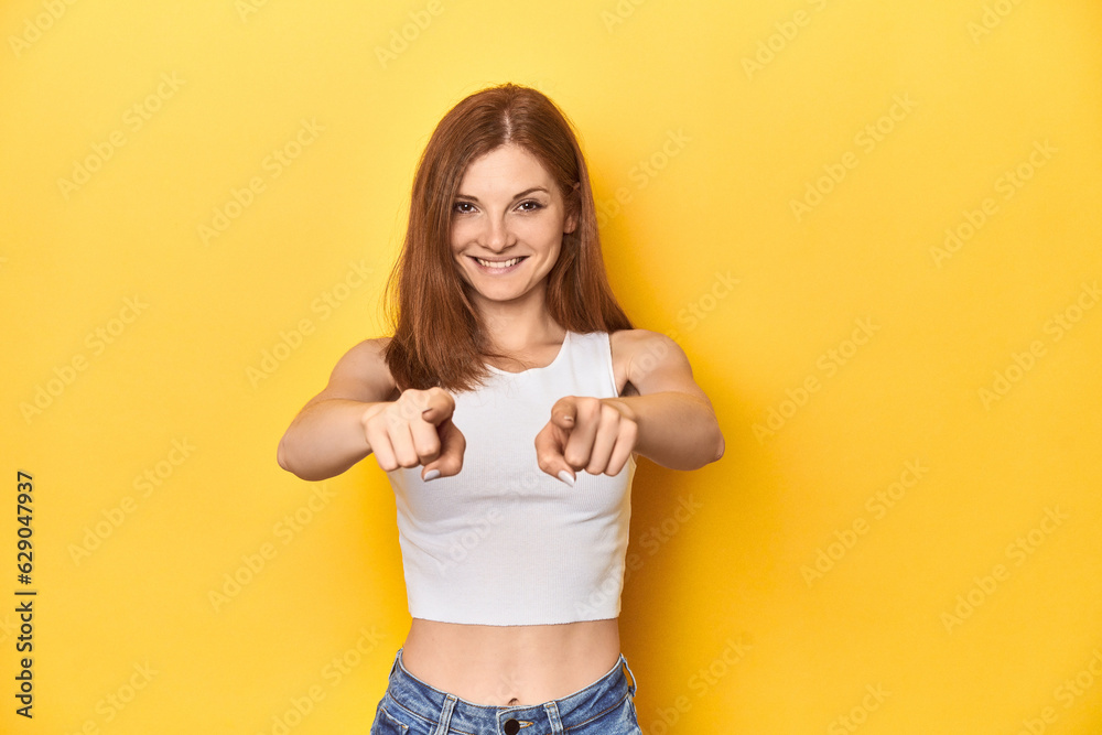 Redhead in white tank top, relaxed studio pose cheerful smiles pointing to front. Redhead in white tank top, relaxed studio pose cheerful smiles pointing to front.