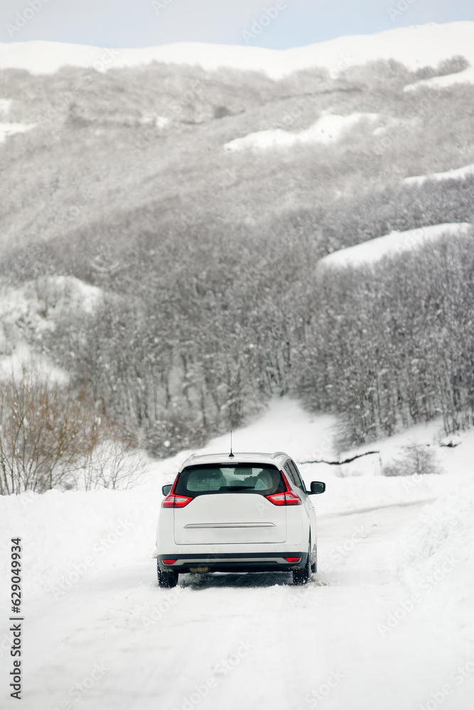 White car riding on a snow-covered road in the European Alps while a snowstorm. Drifts and snow drifts during a snowfall.