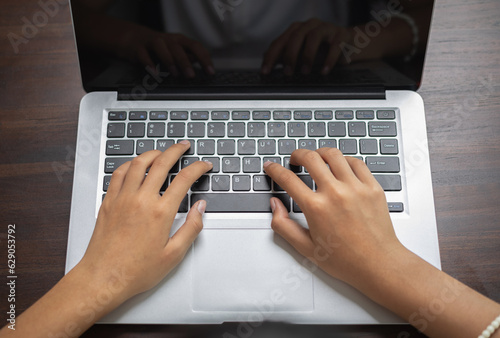 Girl hands using laptop with blank display on wooden desk background. Modern workspace concept.