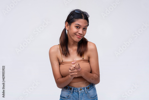 A young asian woman solicits help, looking innocent and sincere. Gesturing with both hands clasped. Isolated on a white background.