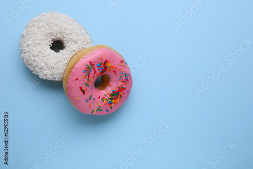 Tasty glazed donuts decorated with coconut shavings and sprinkles on light blue background, flat lay. Space for text